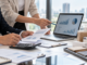 Due professionisti analizzano grafici finanziari e campioni di prodotto per ottimizzare i costi aziendali mantenendo la qualità.